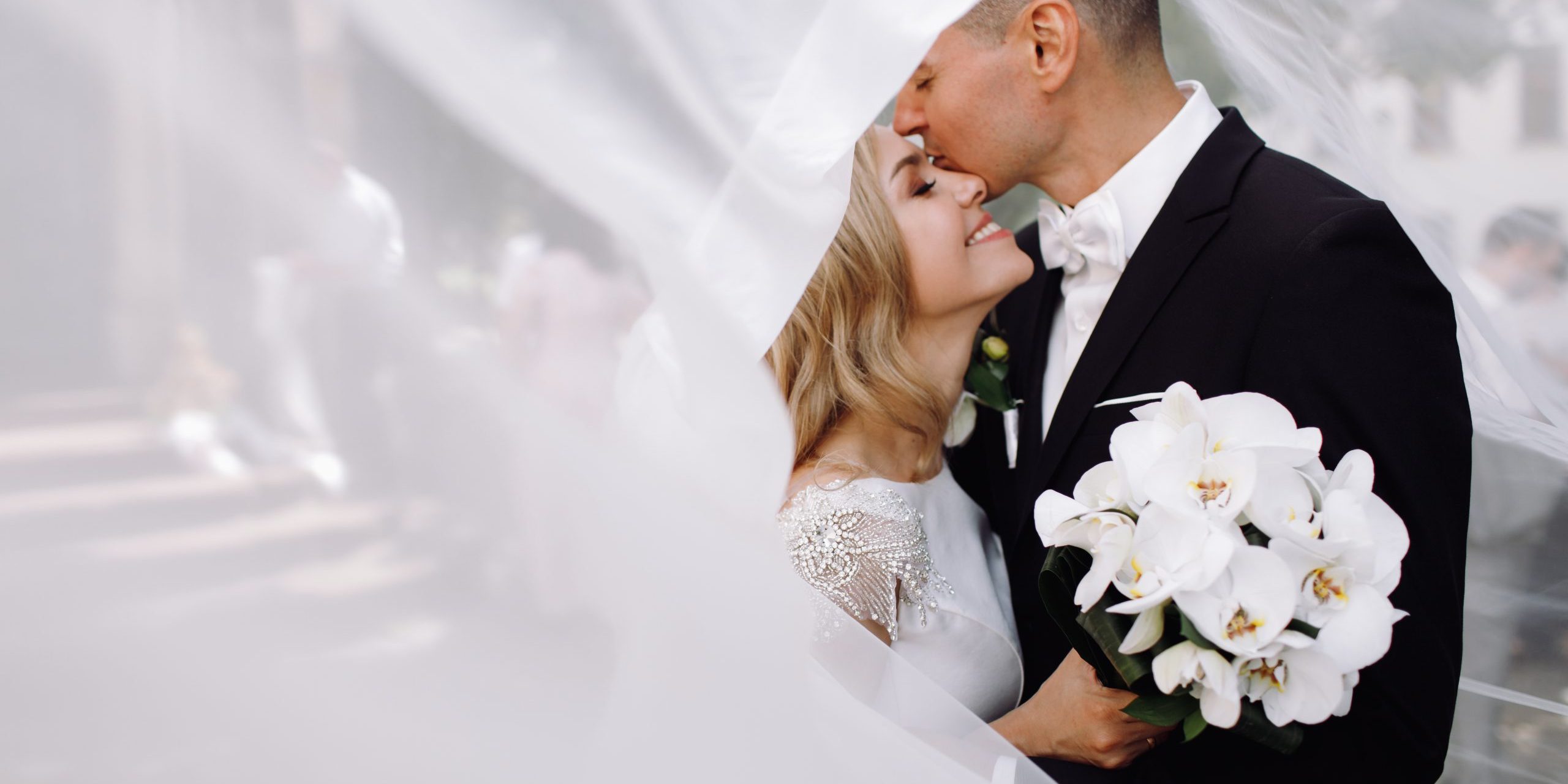 Groom in black tuxedo hugs tender stunning bride while they stan