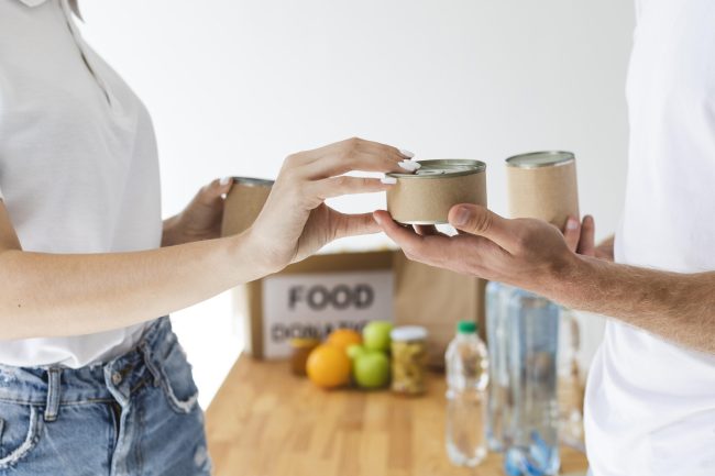 vista-lateral-de-voluntarios-trocando-latas-por-caixas-de-doacao-de-alimentos