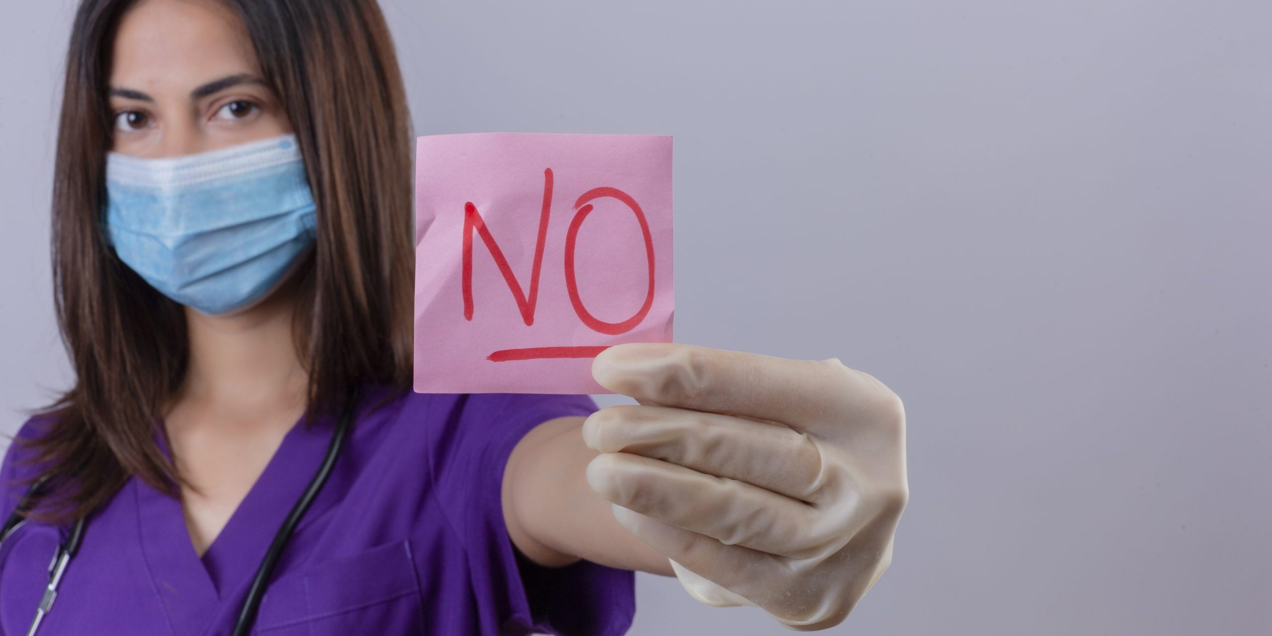 young woman nurse wearing medical uniform protective mask gloves and with stethoscope showing reminder paper with word no looking confident over white background